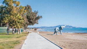 Un paseo marítimo con sendero de hormigón, palmeras y una gran estatua de elefante.