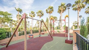 Un parque infantil con columpios, estructuras para escalar y una zona vallada.