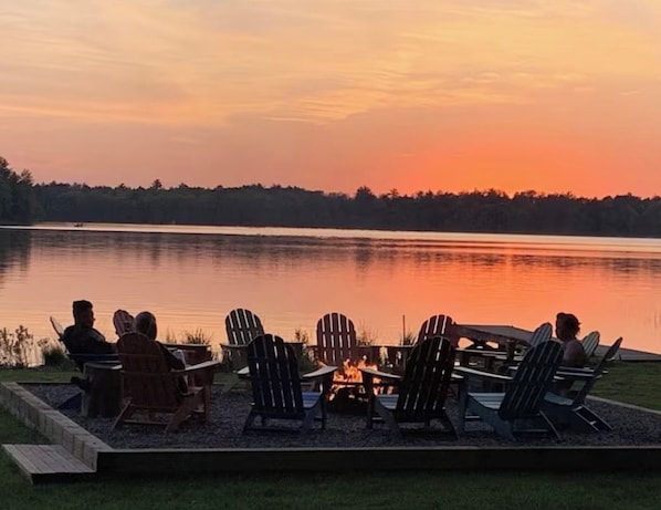 A lakeside seating area with Adirondack chairs and a fire pit.