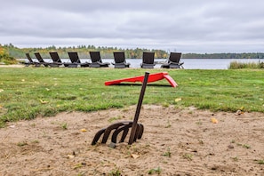 A grassy area with a lake in the background, a red shovel, and several black lounge chairs.