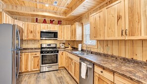 A kitchen with wooden cabinets, stainless steel appliances, granite countertops, and a window with blinds.