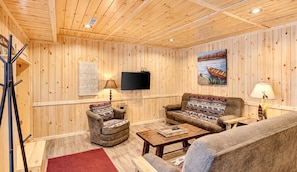 A wooden-paneled room with a sofa, armchair, and a television mounted on the wall.