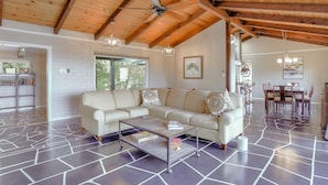 A spacious living area with a sectional sofa, a coffee table, and a dining table set for six. The room features exposed wooden beams, a tiled floor, and large windows allowing natural light. - Skyline Retreat with Spectacular Bay Views (Oakland)