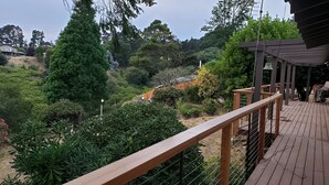 A wooden deck with a railing overlooking a landscaped garden with various plants and trees. - Skyline Retreat with Spectacular Bay Views (Oakland)