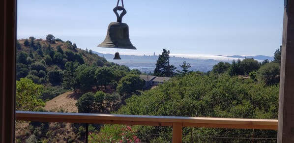A view from a balcony with a hanging bell, a hillside with trees, and a distant cityscape. - Skyline Retreat with Spectacular Bay Views (Oakland)