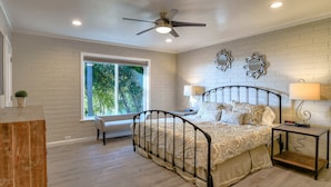 A bedroom with a bed, a bench, a nightstand, a ceiling fan, and a window with a view of trees. - Skyline Retreat with Spectacular Bay Views (Oakland)