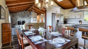 A spacious dining area with a high ceiling and wooden beams, a stone wall, and a modern kitchen with stainless steel appliances. - Skyline Retreat with Spectacular Bay Views (Oakland)