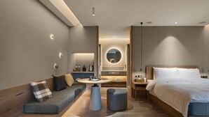 Une chambre d’hôtel moderne avec un lit en bois, une table ronde, un canapé et un petit tabouret.