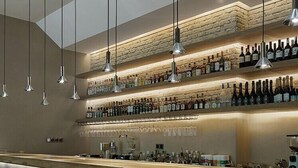 Un bar moderne doté de plusieurs étagères à bouteilles, de luminaires suspendus et d’un long comptoir.