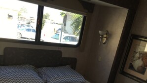 Een bed met een gestoffeerd hoofdeinde, een raam met een 'EXIT' bord en een lijst met een afbeelding aan de muur.