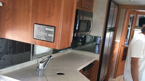 Een keuken met houten kastjes, een roestvrijstalen magnetron en een Kenwood-apparaat op het aanrecht.
