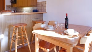 A wooden dining table with chairs, a wine bottle, and glasses on a kitchen island. - Les Arsets 01/203 by Interhome (Alpe des Chaux)