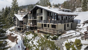 A modern multi-story building with balconies, surrounded by snow-covered trees and a mountainous backdrop. - Les Arsets 01/203 by Interhome (Alpe des Chaux)