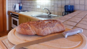A loaf of bread on a wooden cutting board in a kitchen with a tiled backsplash and wooden cabinets. - Les Arsets 01/203 by Interhome (Alpe des Chaux)
