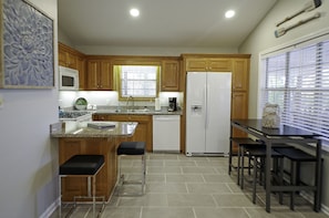 Una cocina con armarios de madera, un refrigerador blanco, un microondas, un fregadero y un comedor con taburetes.