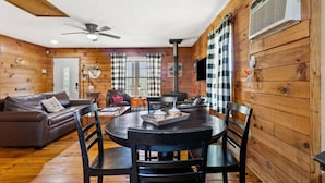 A cozy cabin interior with a wooden interior, a round dining table with chairs, a leather sofa, and a ceiling fan. - Heavenly Hideaway- Hot Tub, Firepit, Covered Patio, WiFi (Beattyville)