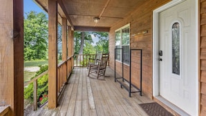 A wooden porch with a white door, a bench, and a view of a green landscape. - Heavenly Hideaway- Hot Tub, Firepit, Covered Patio, WiFi (Beattyville)
