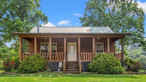 A wooden cabin with a porch, stone foundation, and a metal roof. - Heavenly Hideaway- Hot Tub, Firepit, Covered Patio, WiFi (Beattyville)