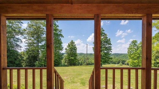 A wooden deck with a view of a grassy field and trees. - Heavenly Hideaway- Hot Tub, Firepit, Covered Patio, WiFi (Beattyville)
