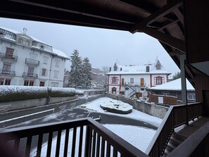 A snow-covered courtyard with a wooden staircase, a snow-covered tree, and buildings with balconies.