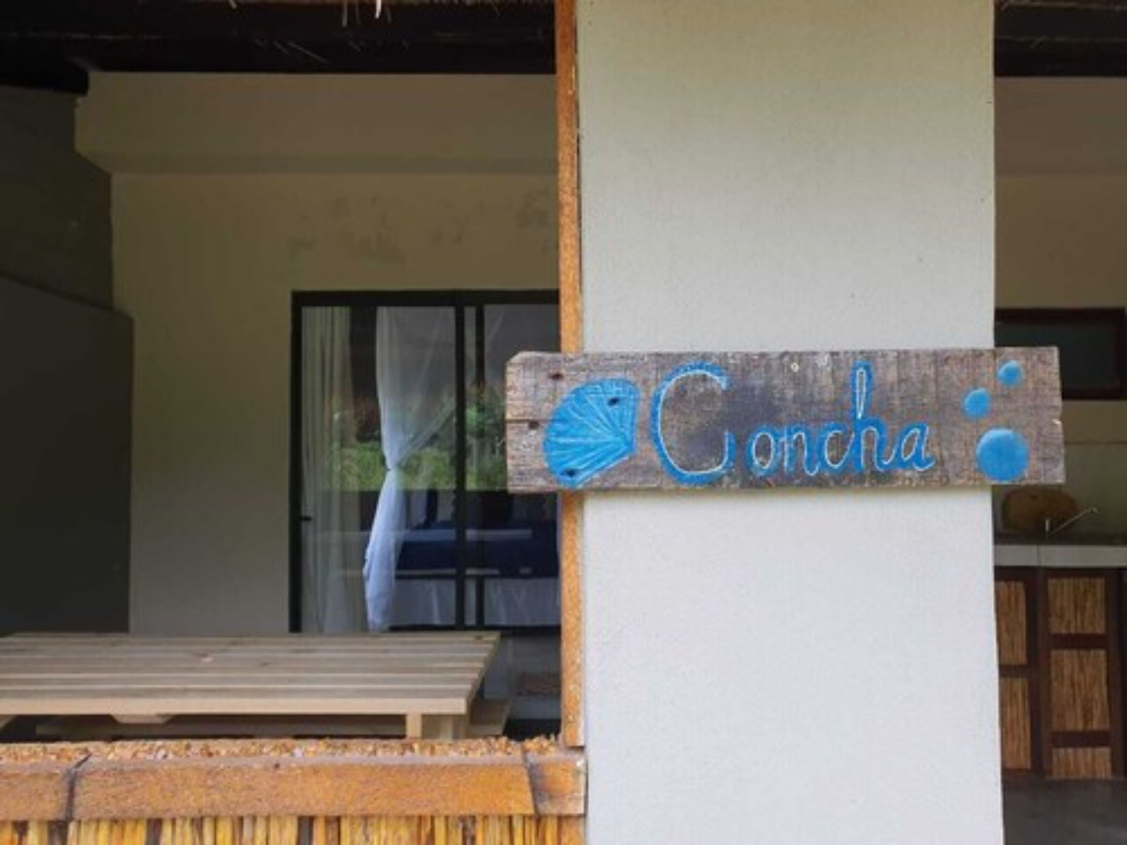 Een houten bord met de naam 'Concha' en een blauwe sint-jakobschelp, wat een strand- of kustthema aangeeft.