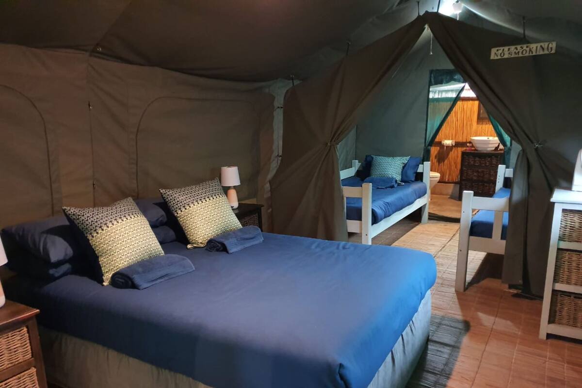 A tented accommodation with a bed, pillows, a lamp, and a 'No Smoking' sign.