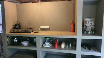 Eine Küche mit Gaskochfeld, Wasserkocher, Feuerlöscher und Regalen mit Küchenutensilien.
