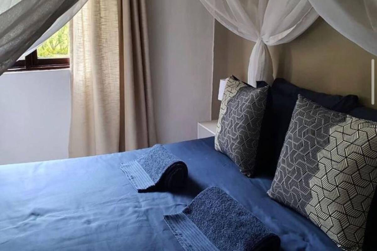 A bed with a canopy, patterned pillows, and a window with curtains.