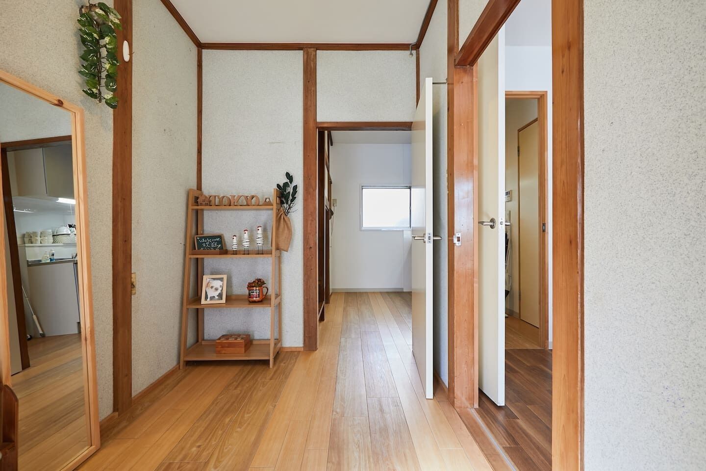 A hallway with wooden flooring and a shelf with decorative items.