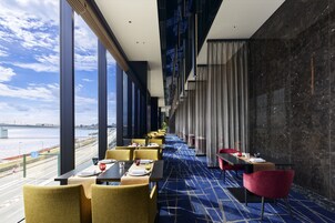 A restaurant with a view of the river, tables set with plates and glasses, and a blue carpet.