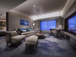 A modern hotel room with a sofa, ottoman, coffee table, and TV.