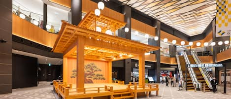 A modern indoor space with a central wooden structure, escalators, and a tiled floor.