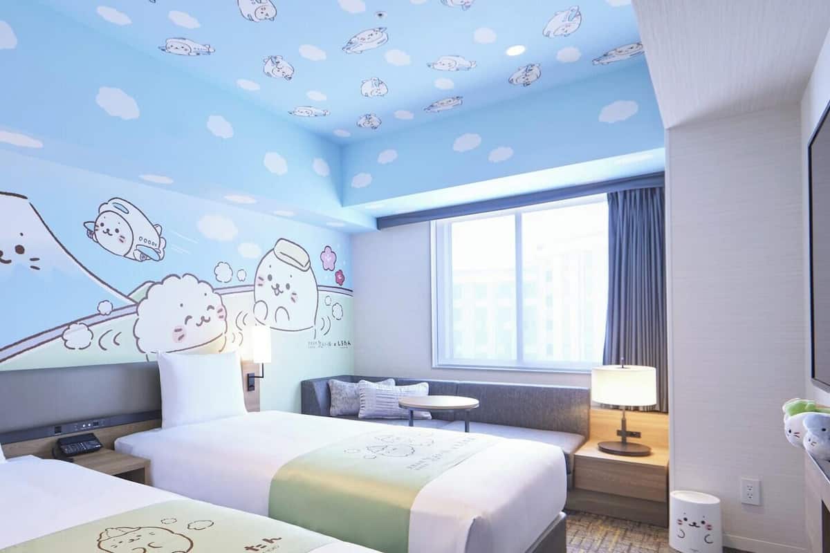 Ein Hotelzimmer mit zwei Betten, einem Schreibtisch, einem Stuhl, einem Fernseher und einem Fenster.