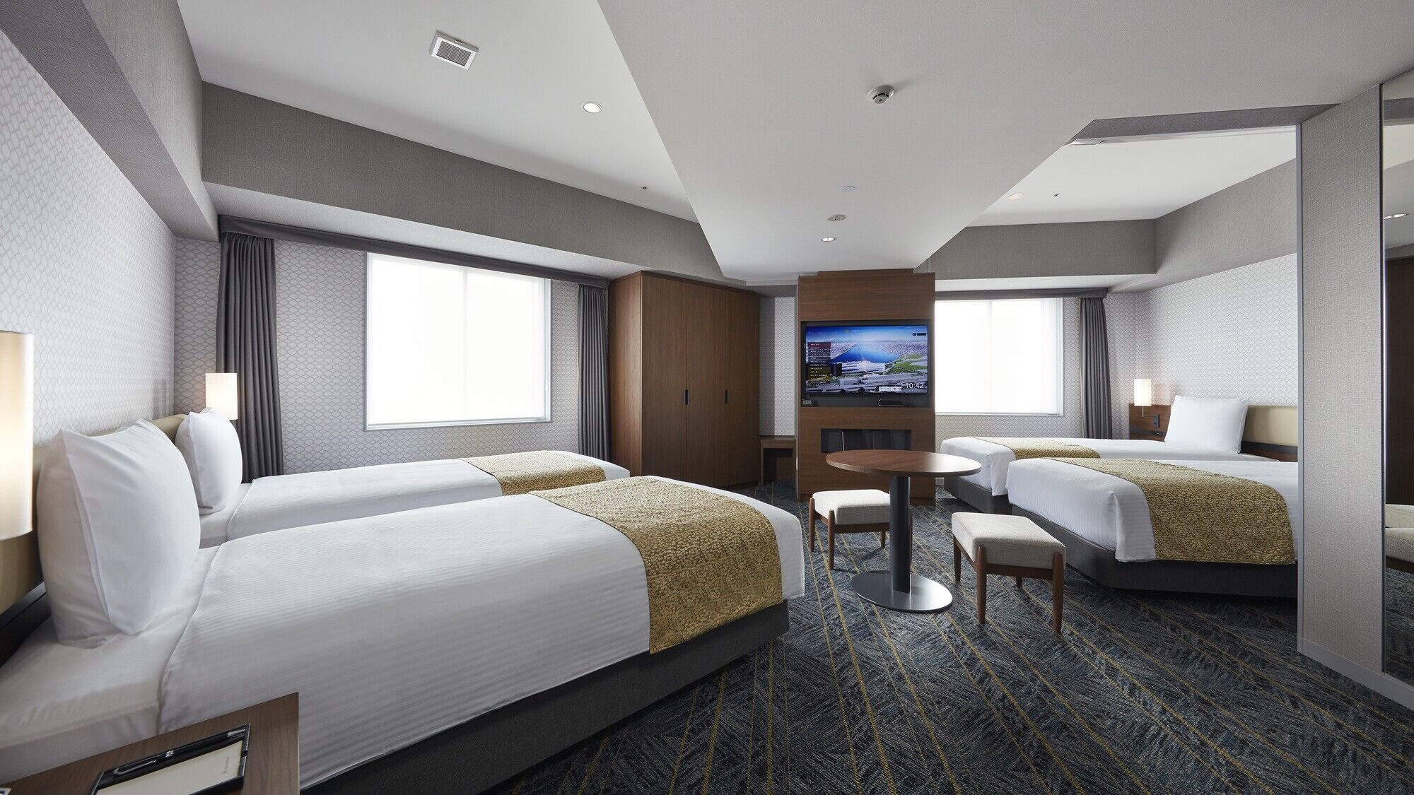 A hotel room with two beds, a TV, a desk, and a large window.