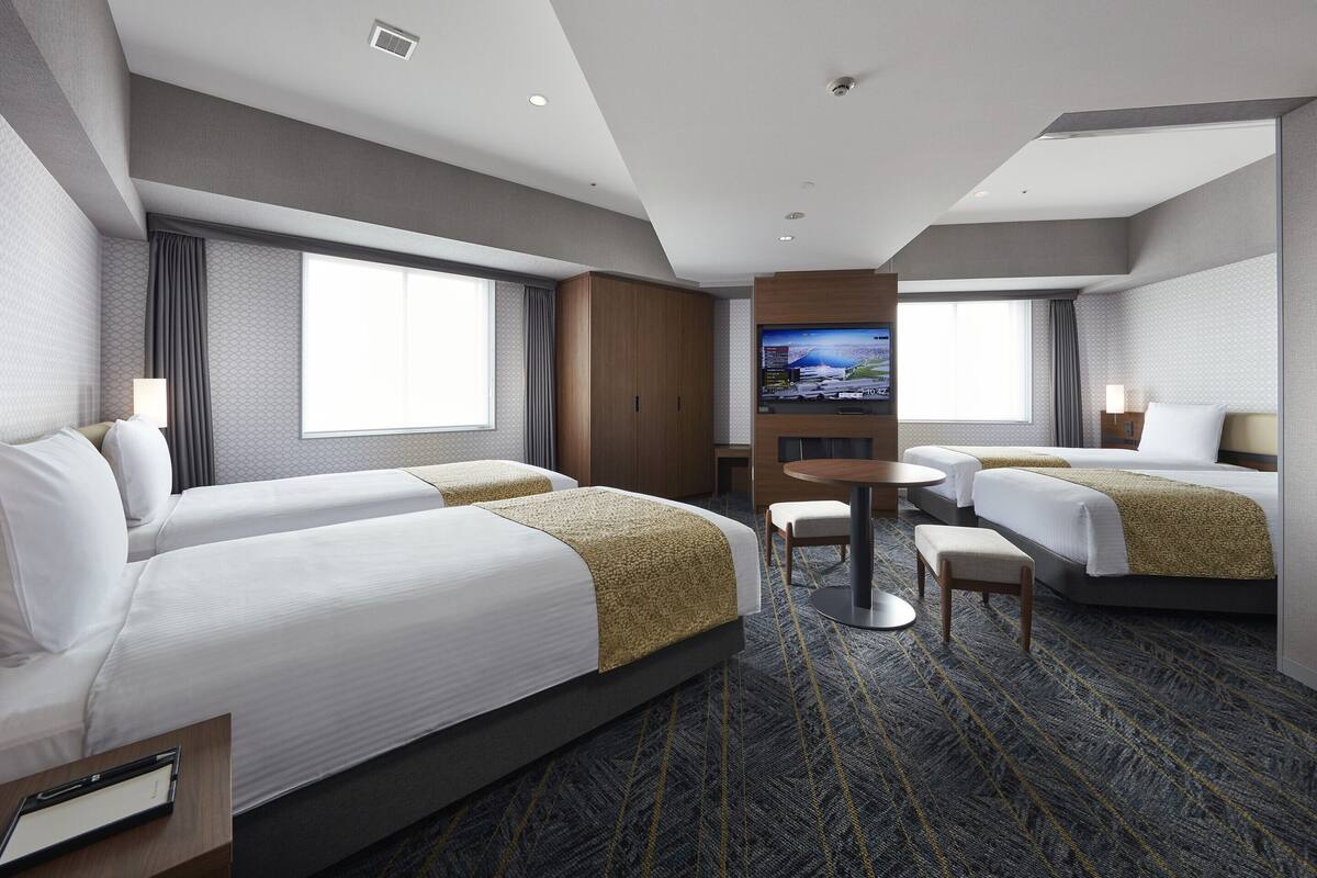 Ein Hotelzimmer mit zwei Betten, einem Fernseher, einem kleinen Tisch und einer Sitzecke.