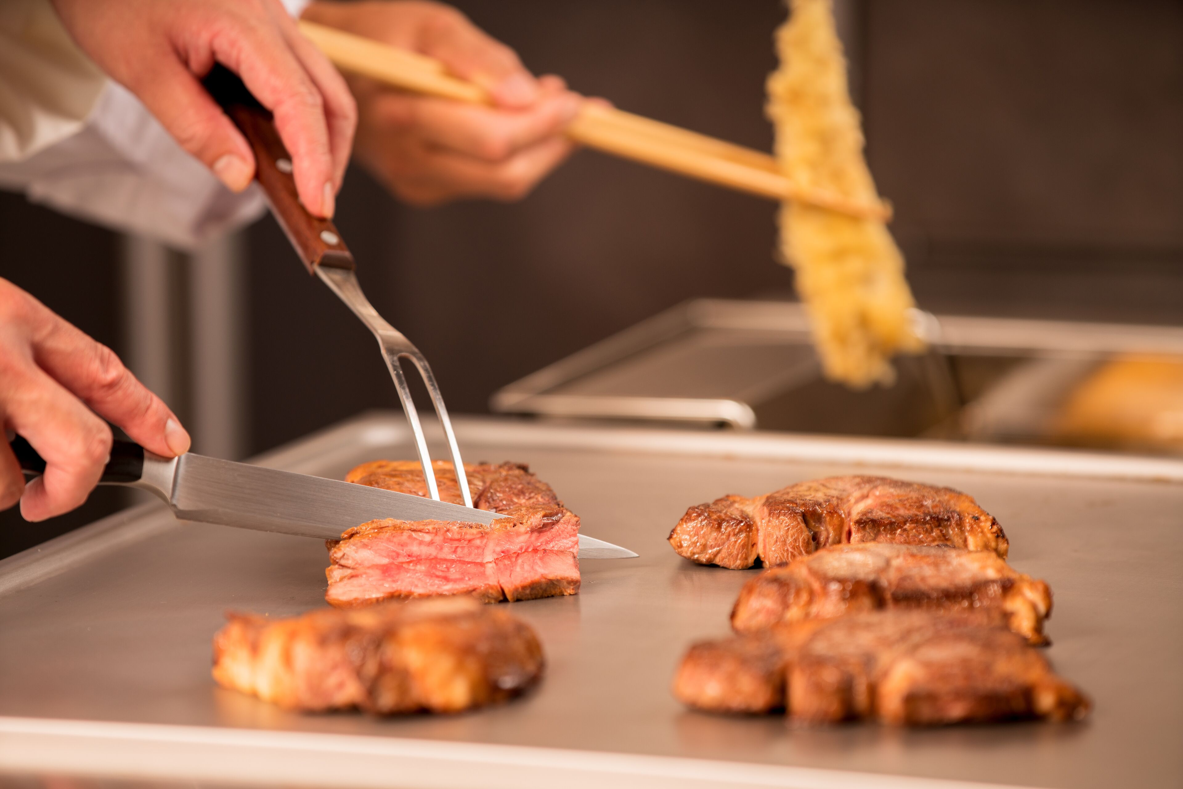 Una persona cortando carne en una parrilla.