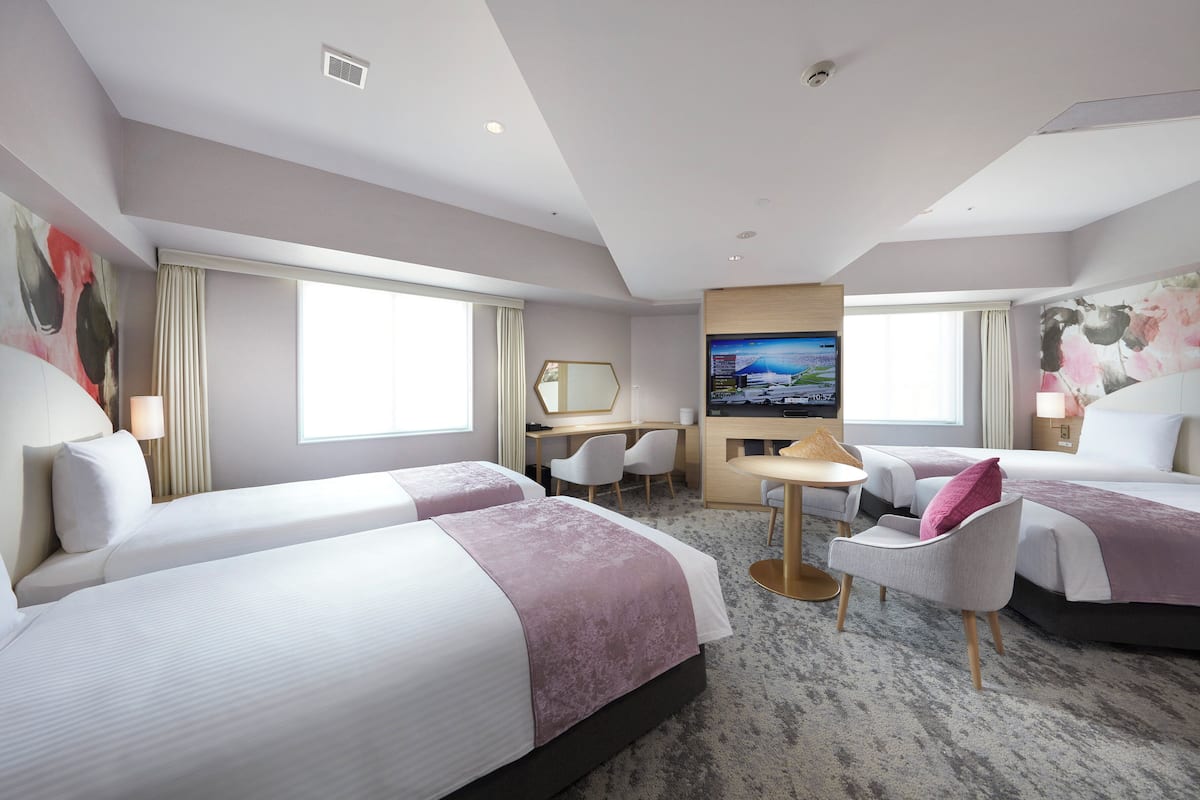 Ein Hotelzimmer mit zwei Betten, einem Schreibtisch, einem Fernseher und einer Sitzecke.
