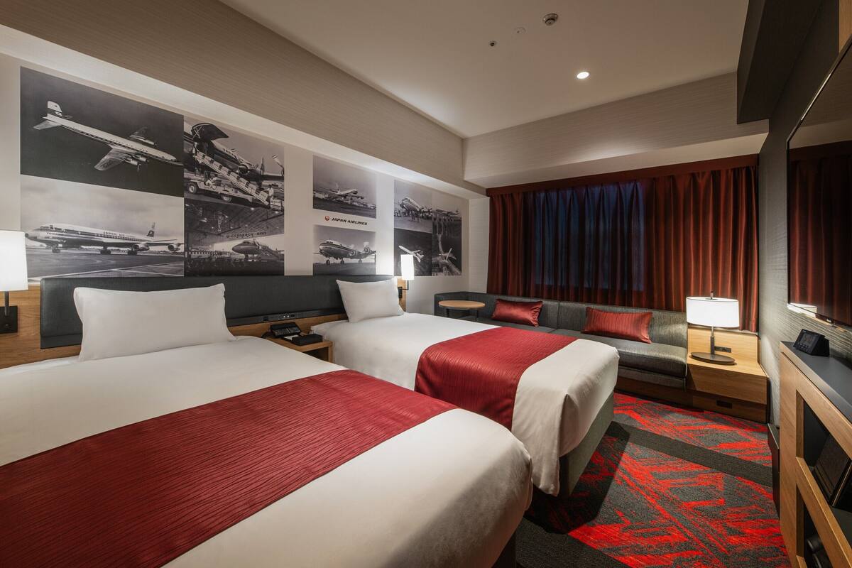 Ein Hotelzimmer mit zwei Betten, einem Schlafsofa, einem kleinen Tisch und einem Fernseher.