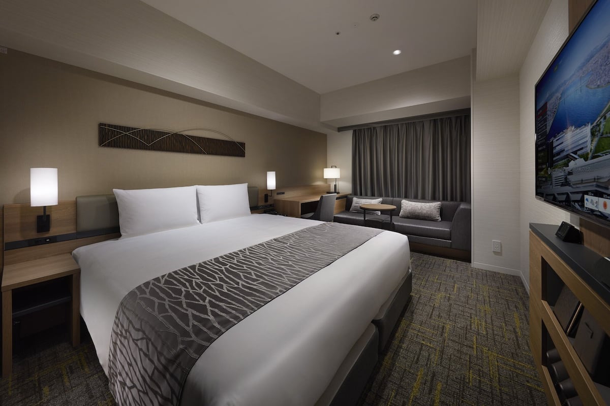 Ein modernes Hotelzimmer mit einem großen Bett, einer Sitzecke, einem Schreibtisch und einem Flachbildfernseher.