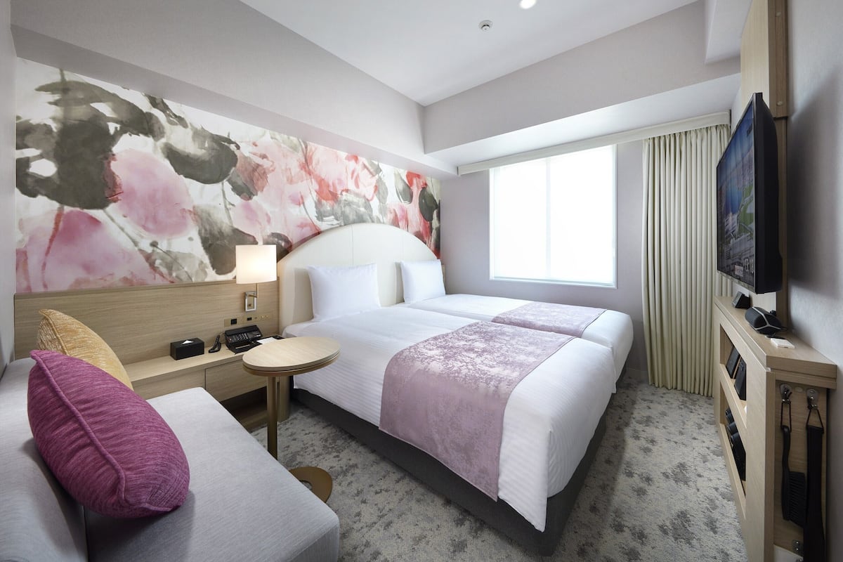 Ein Hotelzimmer mit einem großen Bett, einem Schreibtisch, einem Stuhl, einem Fernseher und einem Gemälde an der Wand.