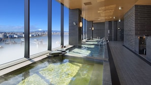 Ein moderner, überdachter Pool mit freiem Blick auf eine Stadtlandschaft und ein Gebirge.