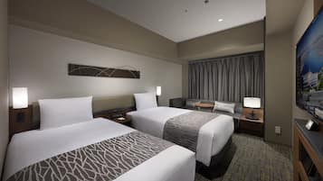 A hotel room with two beds, a desk, a TV, and a large window with curtains.