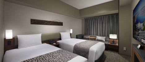 A hotel room with two beds, a desk, a TV, and a large window with curtains.