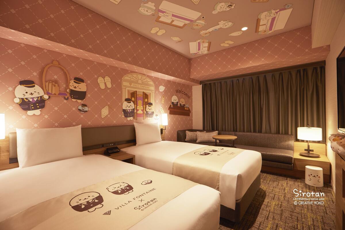 Ein Hotelzimmer mit zwei Betten, einem Schlafsofa, einem Schreibtisch und einem Badezimmer.
