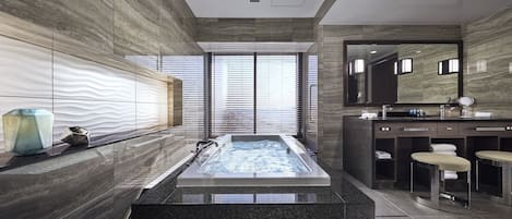 Un bagno moderno con una grande vasca da bagno rettangolare, un mobile lavabo con specchio e un'area salotto con degli sgabelli.