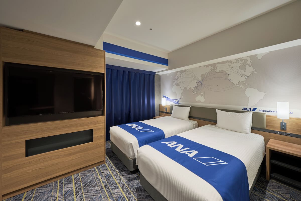 Ein Hotelzimmer mit zwei Betten, einem Fernseher, einer Weltkarte an der Wand und einem Holzschrank.
