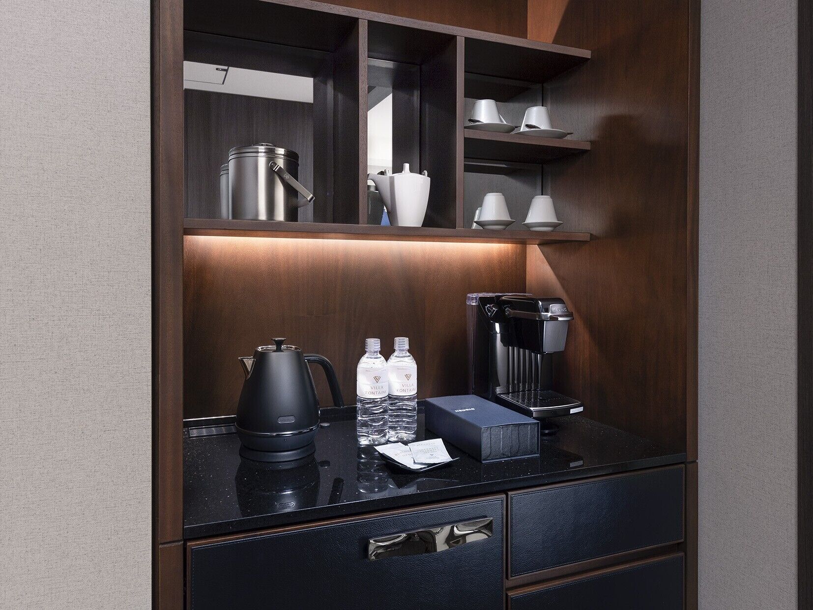 A modern, well-lit kitchenette with a coffee maker, water bottles, and a kettle.