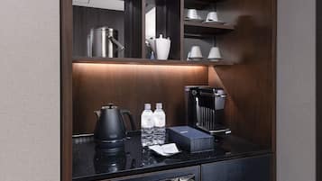 A modern, well-lit kitchenette with a coffee maker, water bottles, and a kettle.