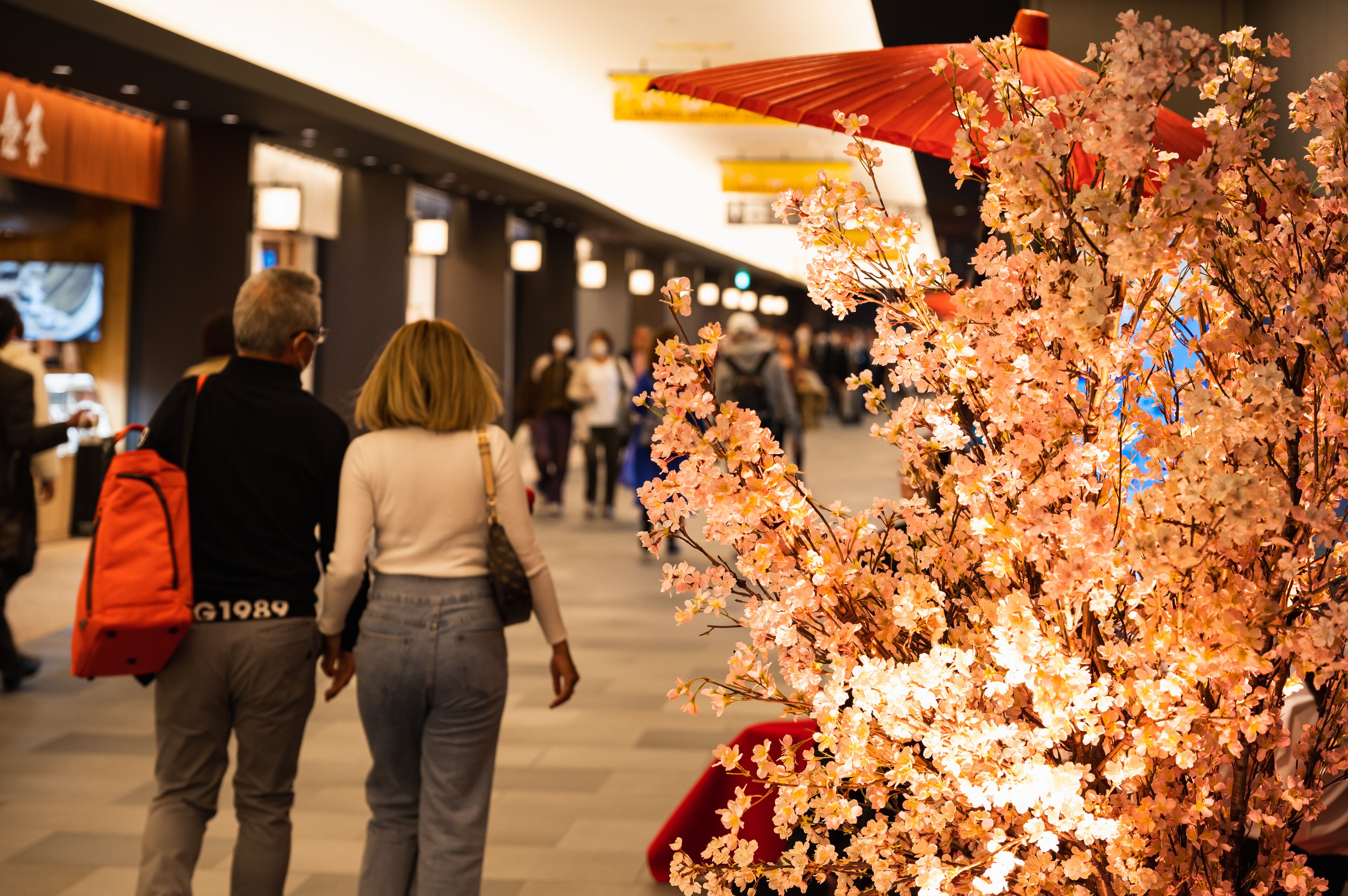 A corridor with a cherry blossom display and a red umbrella.