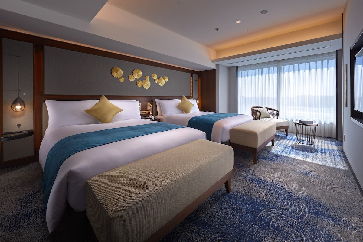 Ein Hotelzimmer mit zwei Betten, einer Sitzecke und einem großen Fenster mit Vorhängen.